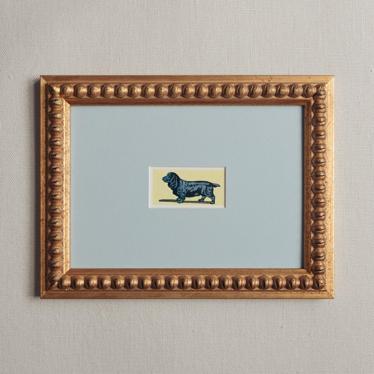 Handmade bobbin frame in antique style gold with blue mount, framing a mid century image of a black Spaniel on a yellow background. Only available at Giddy Prints. 